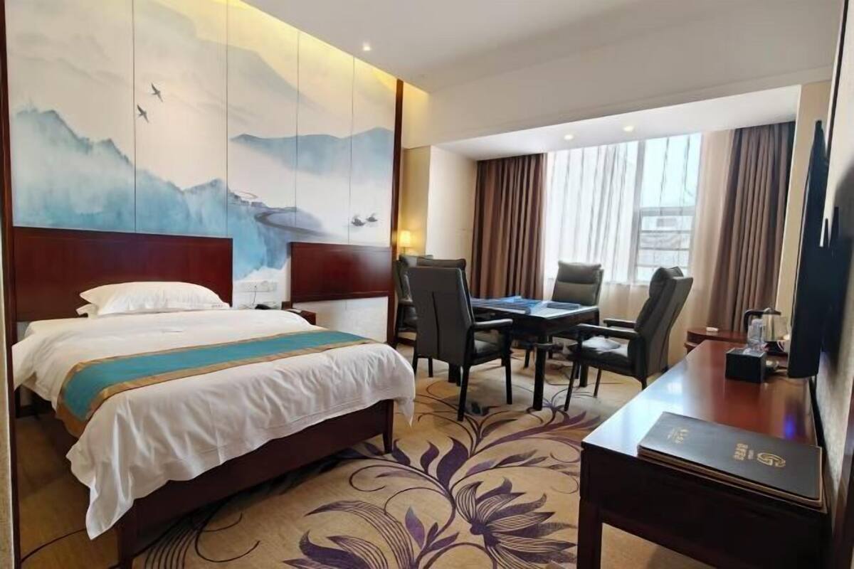 A hotel room with a bed, a desk, a chair, a television, and a painting on the wall.