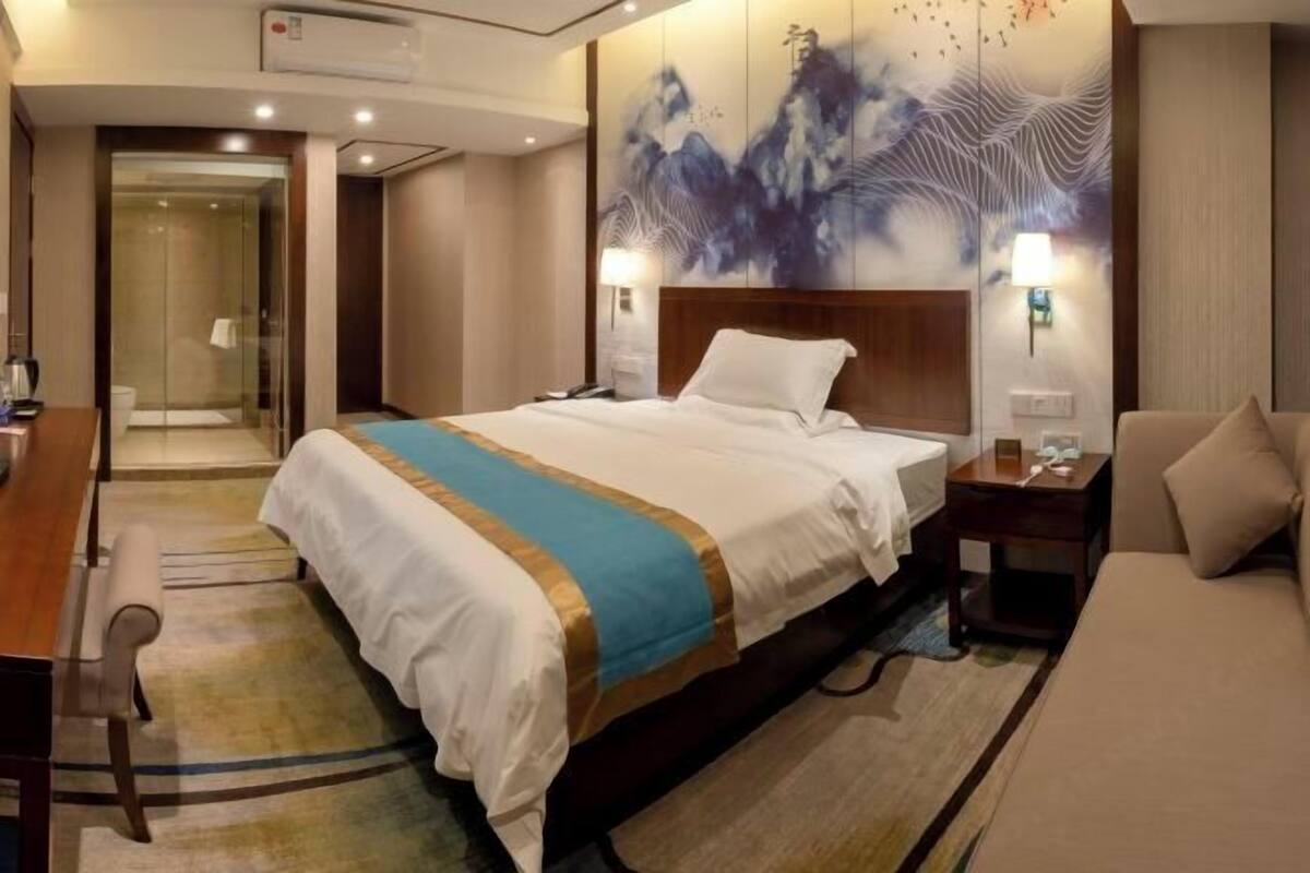 A hotel room with a large bed, a desk, a chair, a sofa, and a wall with artwork.