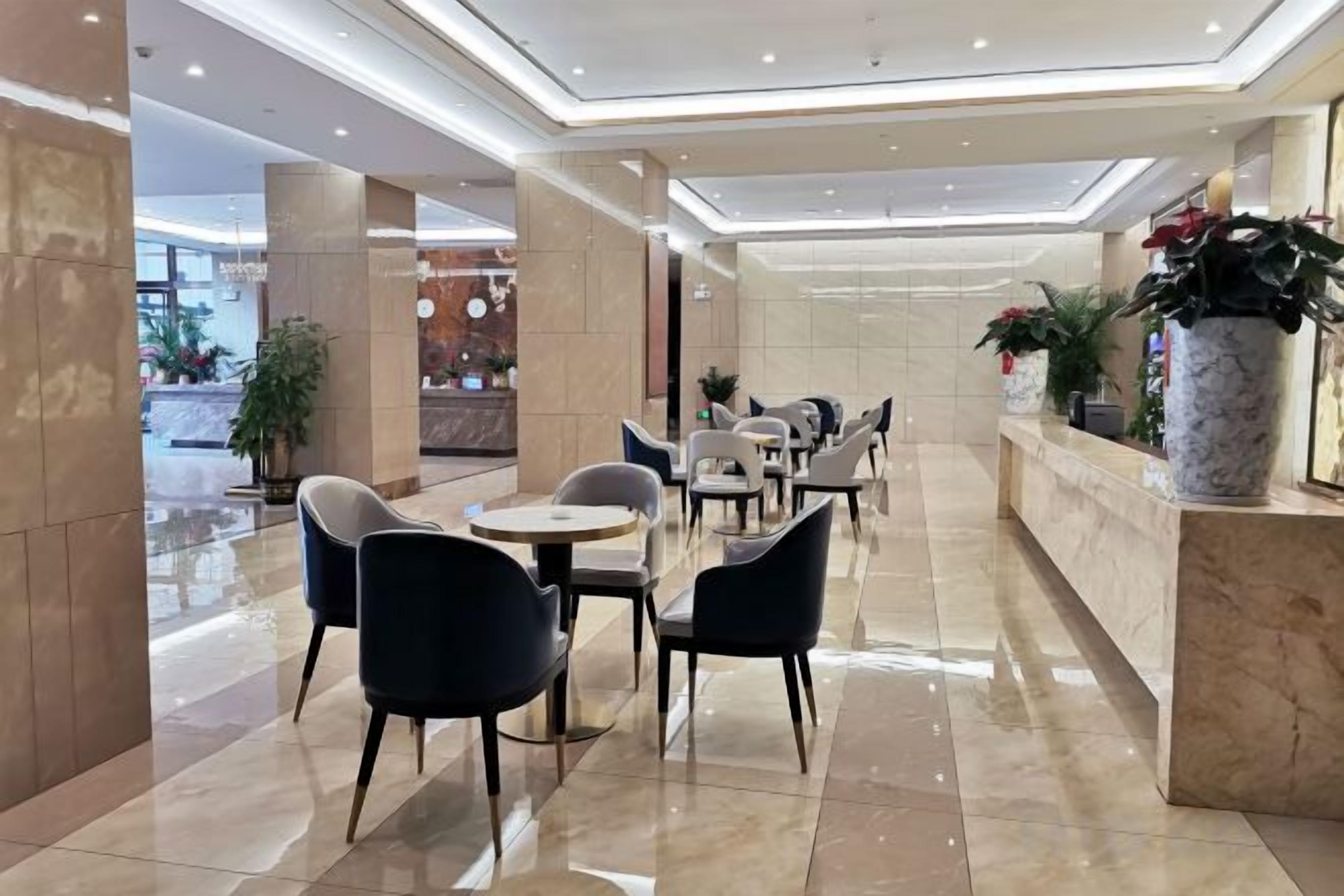 A hotel lobby with a reception desk, seating area, and potted plants.