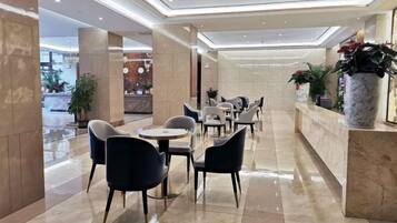 A hotel lobby with a reception desk, seating area, and potted plants.