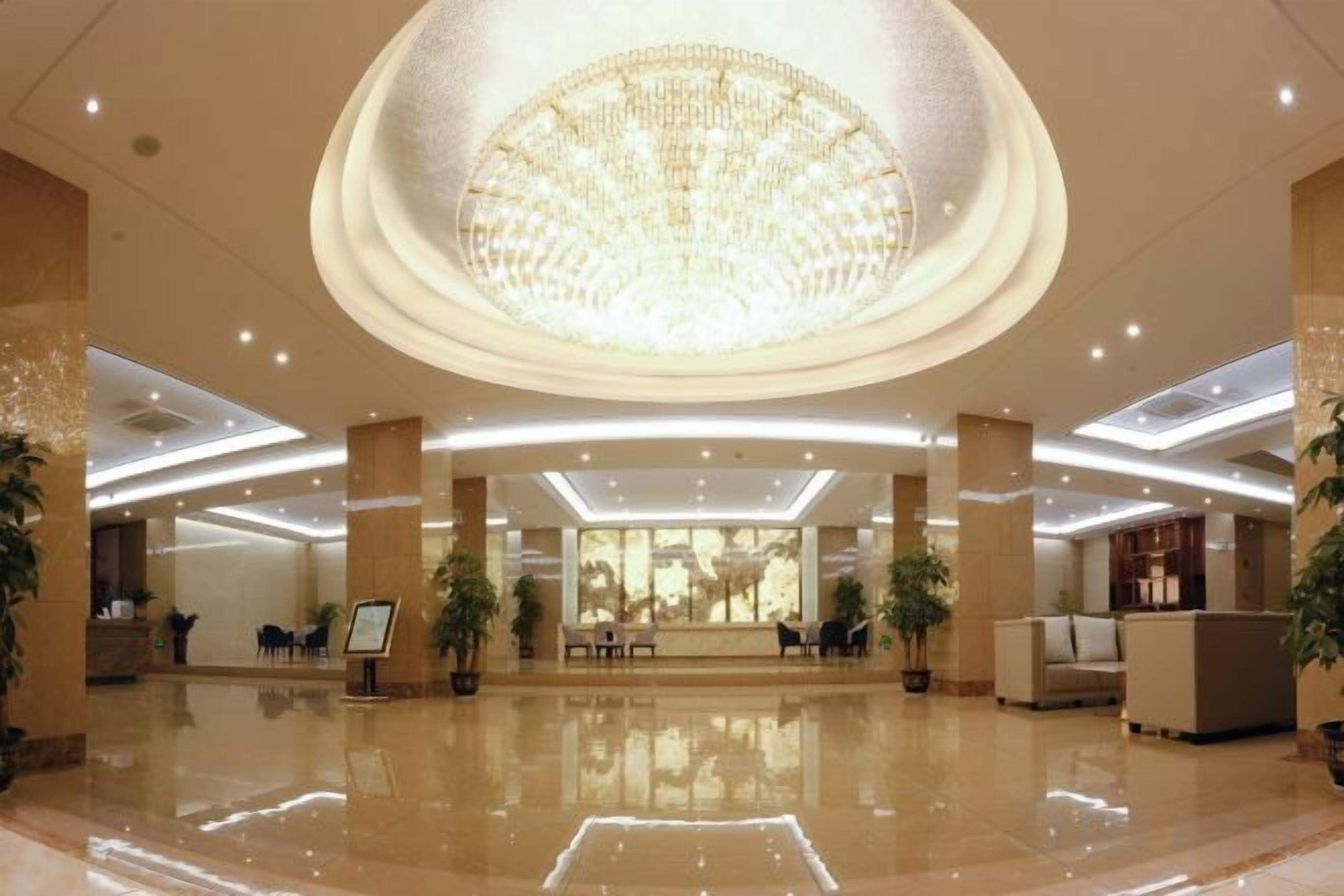 A spacious lobby with a large chandelier, reception desk, and seating area.