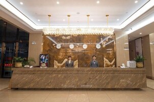 Un mostrador de recepción con encimera de mármol, dos empleados, una araña de cristal y un mural grande en la pared.