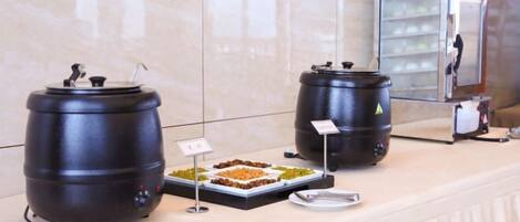A buffet setup with two large black containers, a refrigerated display case, and a tray of food.