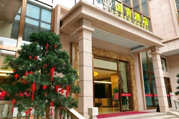 A hotel entrance with a large glass door, a red carpet, and a Christmas tree with red ornaments.