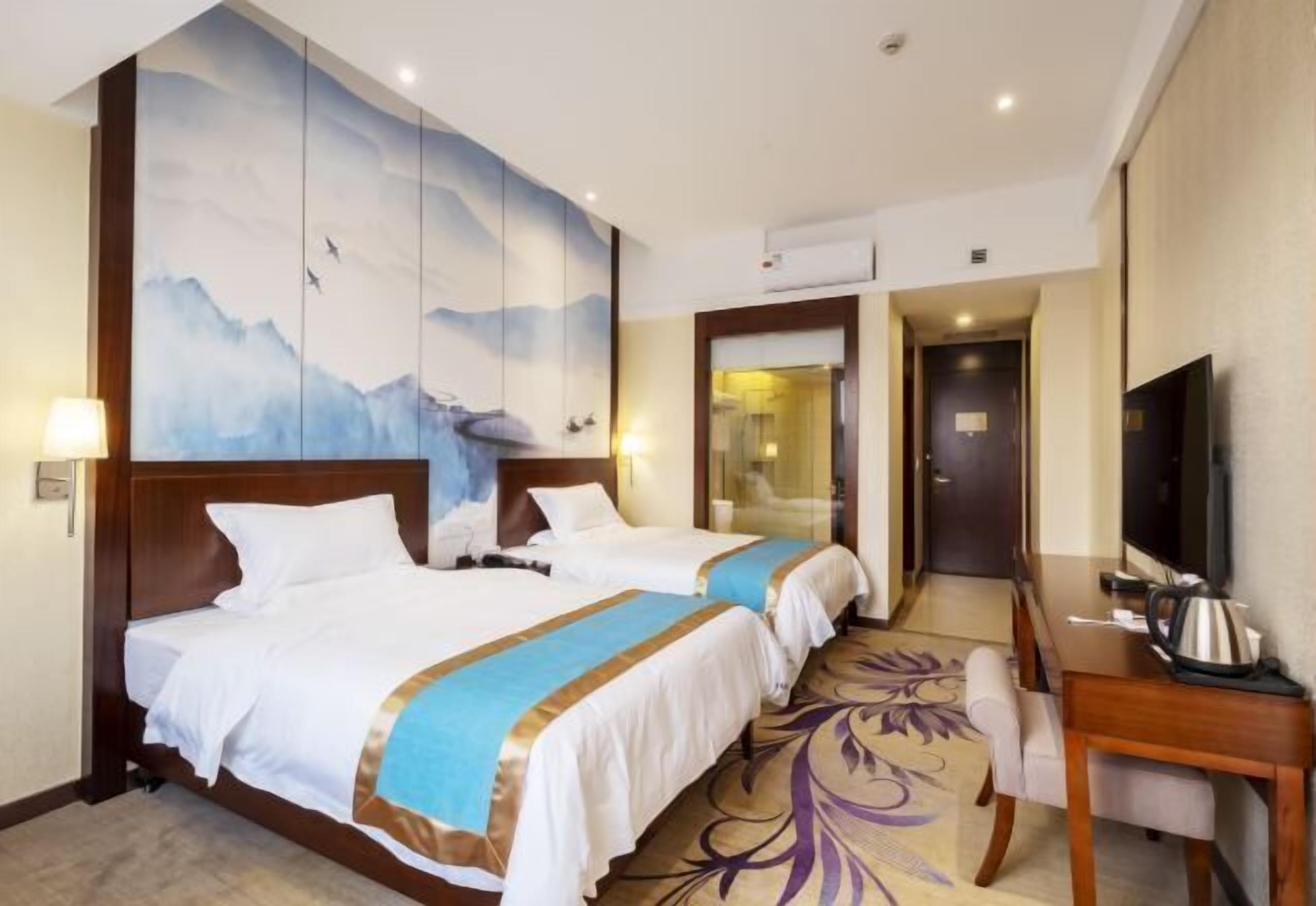 Habitación de hotel con dos camas, un mural grande en la pared, un escritorio con televisor y una puerta que da a un baño.