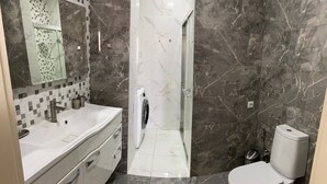 Une salle de bain moderne avec un sol en marbre, un lavabo blanc, un miroir et des toilettes.