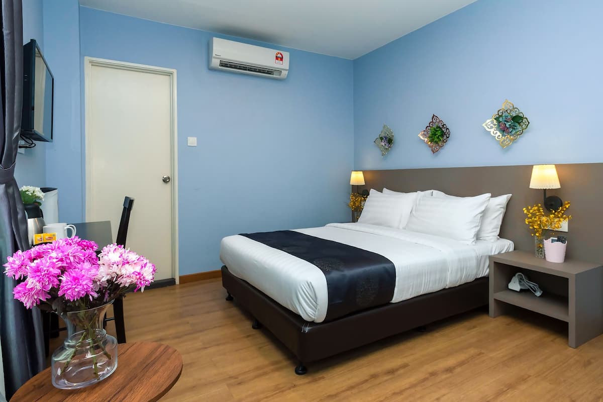 A hotel room with a bed, bedside tables, a TV, an air conditioner, and a vase with flowers.