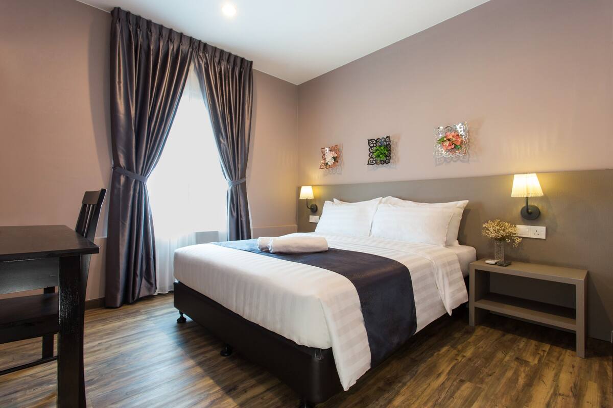 A neatly arranged hotel room with a bed, bedside tables, a desk, and a window with curtains.