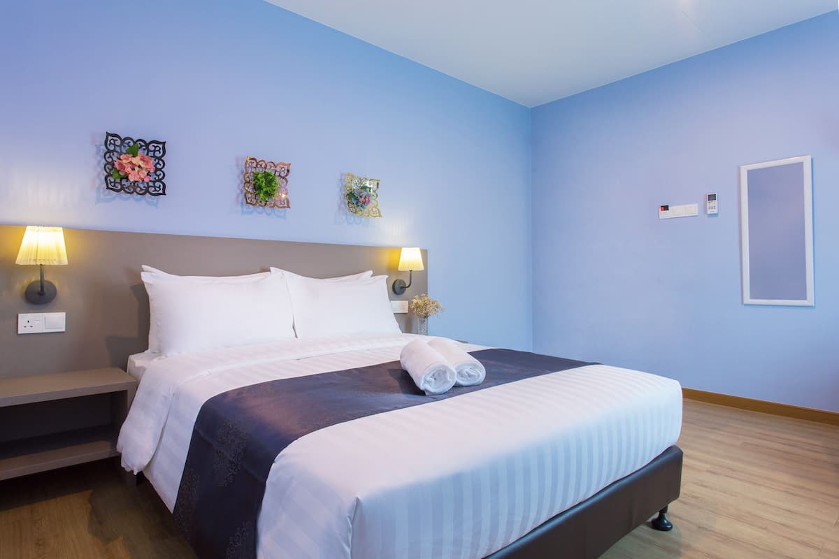 A neatly made bed with white linens and a folded towel, a bedside table with a lamp, and decorative wall art.
