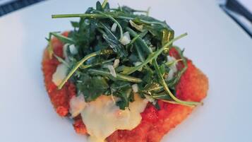 A square plate with a red food item topped with green leaves and cheese.