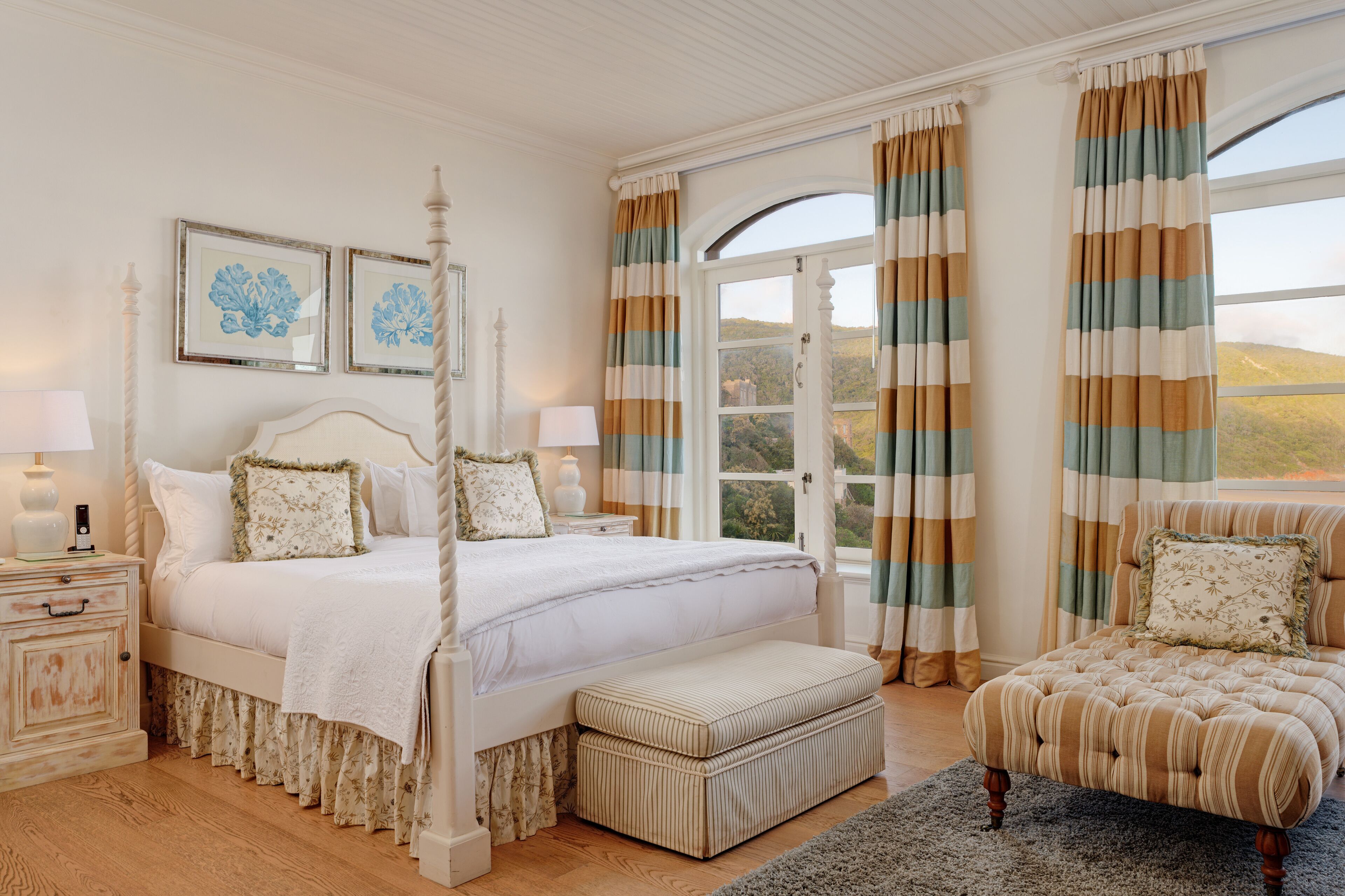 A bedroom with a four-poster bed, a nightstand, a chair, and a view of the outdoors through a window.