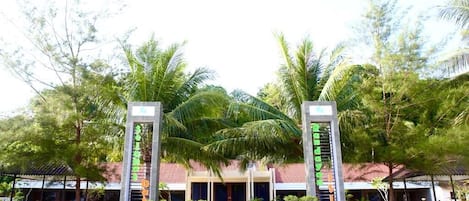 A hotel entrance with a covered walkway, palm trees, and a building with a red roof.