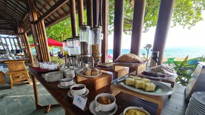 En buffet med forskellige retter og en kaffestation, med udsigt til en strand.