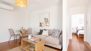 En moderne stue med en sofa, to fletstole, et glasbord og et maleri med ørkenmotiv på væggen.