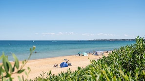 A beach with clear skies, calm waters, and a distant shoreline.