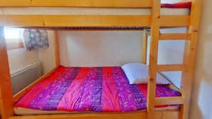 Una cama litera con una colcha de colores morados y rojos, y una almohada blanca.