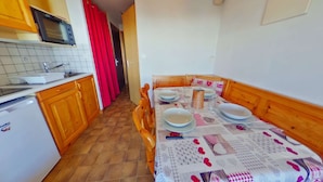 Cocina compacta con armarios de madera, microondas y pileta. Una mesa de comedor con platos y vasos está colocada en el centro.