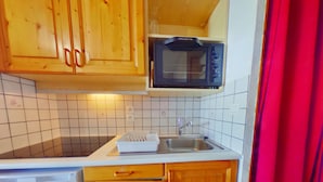 Una cocina compacta con armarios de madera, microondas, fregadero y lavavajillas.