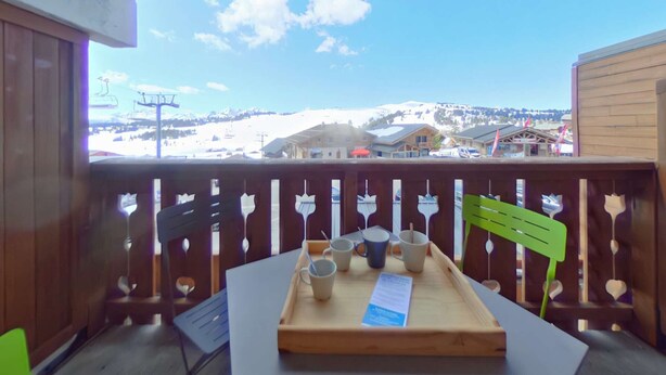 Un balcón con baranda de madera, una mesa con una bandeja de vasos y un menú, y vistas a un paisaje montañoso nevado.