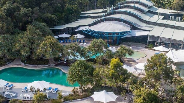 An aerial view of a resort with a swimming pool, lounge chairs, and a covered area with umbrellas.