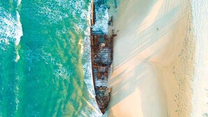 An aerial view of a beach with a large shipwreck on the shore.