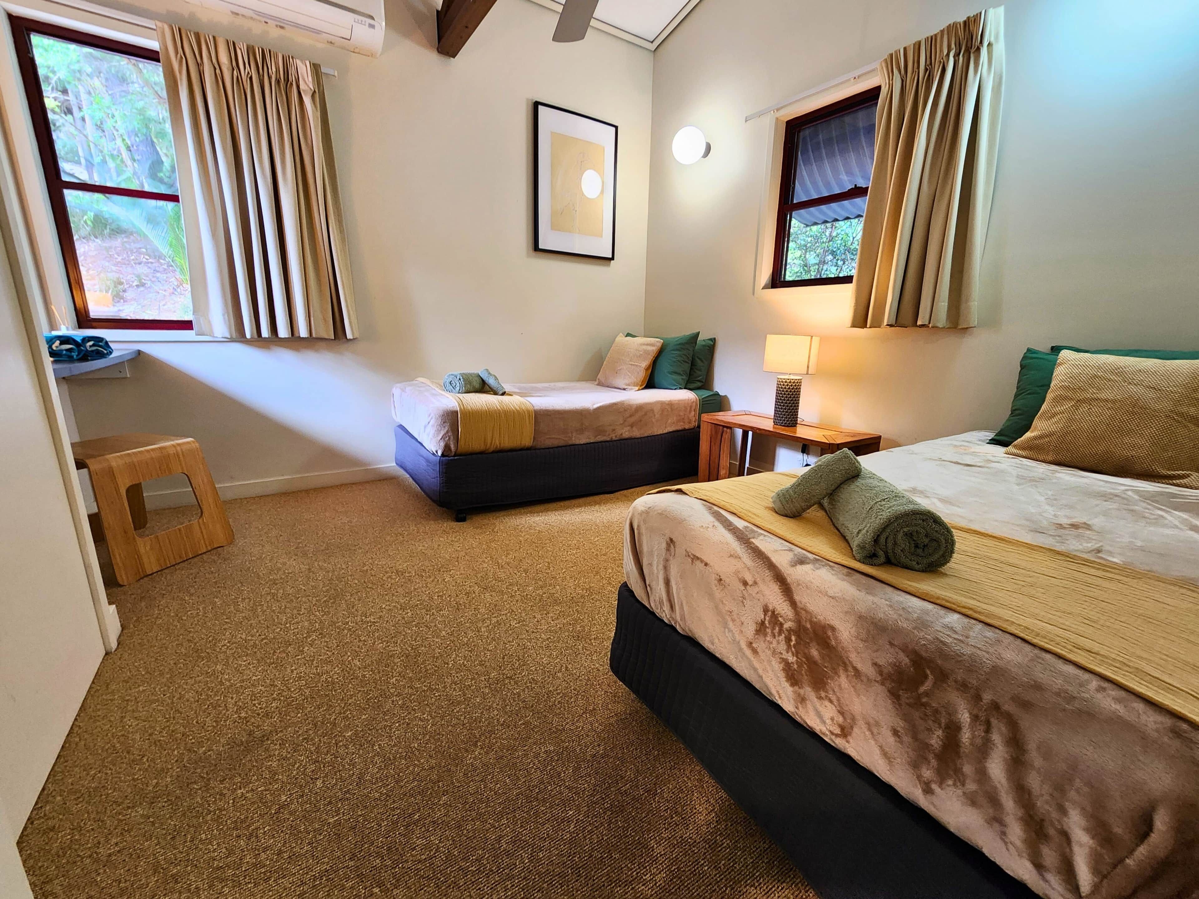 A hotel room with two beds, a small table, a lamp, and a framed picture on the wall.