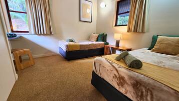 A hotel room with two beds, a small table, a lamp, and a framed picture on the wall.