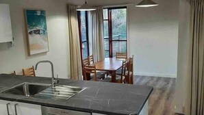 A modern kitchen with a large island, a dining area with a table and chairs, and a view through the windows.