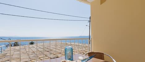 A balcony with a view of the sea, a table with a glass, a bottle, and a blue container.