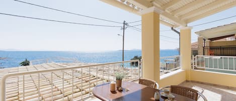 A balcony with a view of the sea, a table with chairs, and a potted plant.