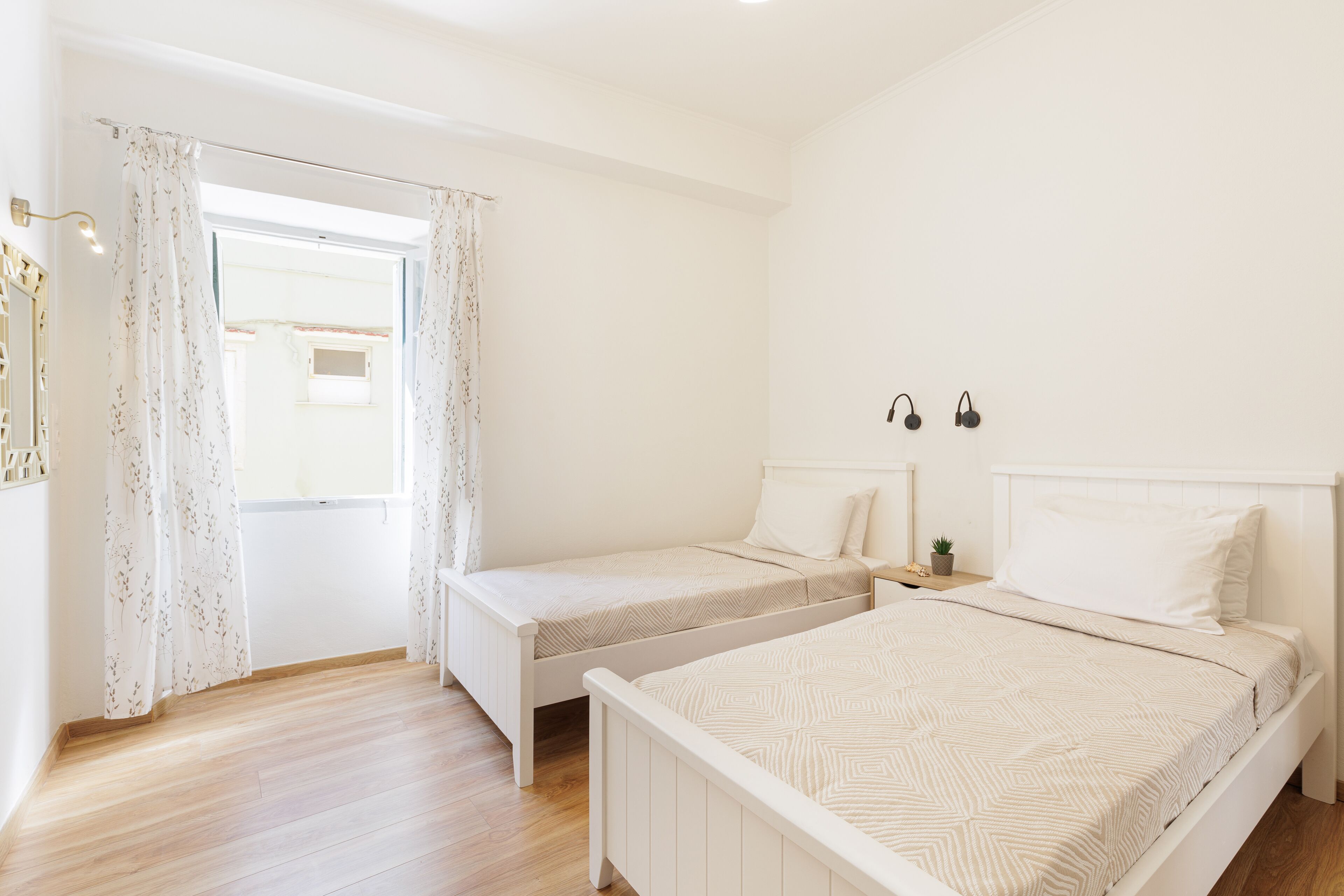 Ein Schlafzimmer mit zwei Einzelbetten, einem kleinen Nachttisch mit Lampe und einem Fenster mit Vorhängen.