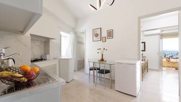 Una cocina moderna con un frutero, un refrigerador y una zona de comedor con una mesa y sillas de vidrio.