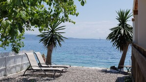 A beachside view with two lounge chairs, a wooden fence, and a palm tree. - Salt and Sun Apartments by Konnect, Kaminaki Beach (Corfu)