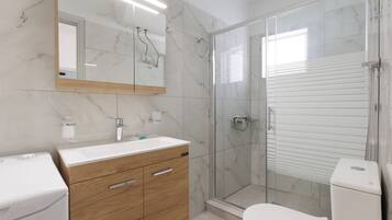 A modern bathroom with a marble backsplash, a wooden vanity, a glass shower enclosure, and a toilet.