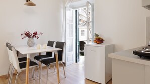 A modern kitchen with a white table, black chairs, a small fridge, and a vase with red flowers. - Salt and Sun Apartments by Konnect, Kaminaki Beach (Corfu)