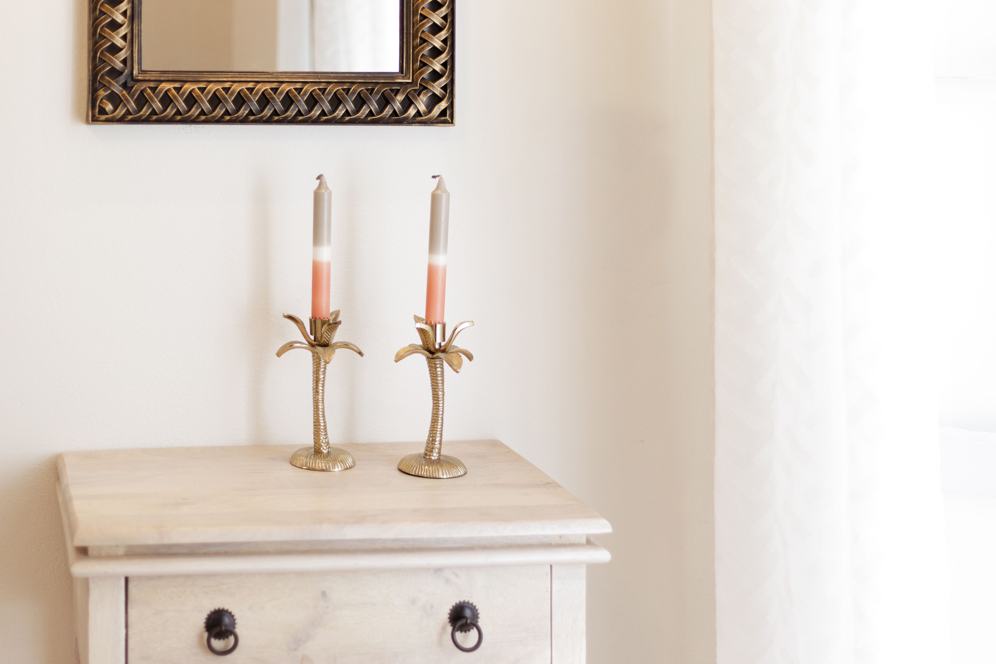 A white dresser with two golden candle holders and candles.