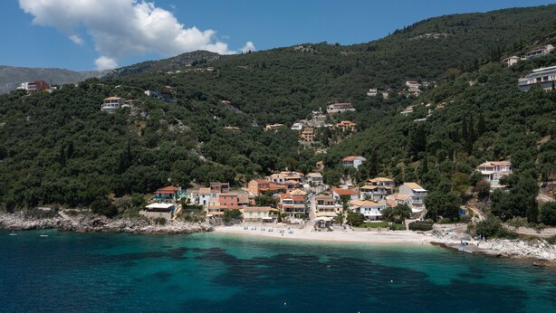 A coastal town with buildings on a hillside, a beach, and clear blue waters. - Salt and Sun Apartments by Konnect, Kaminaki Beach (Corfu)