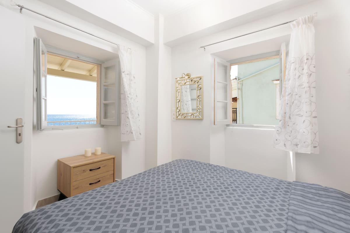Une chambre à coucher avec un lit, une commode en bois, une fenêtre donnant sur un beau paysage et un miroir.