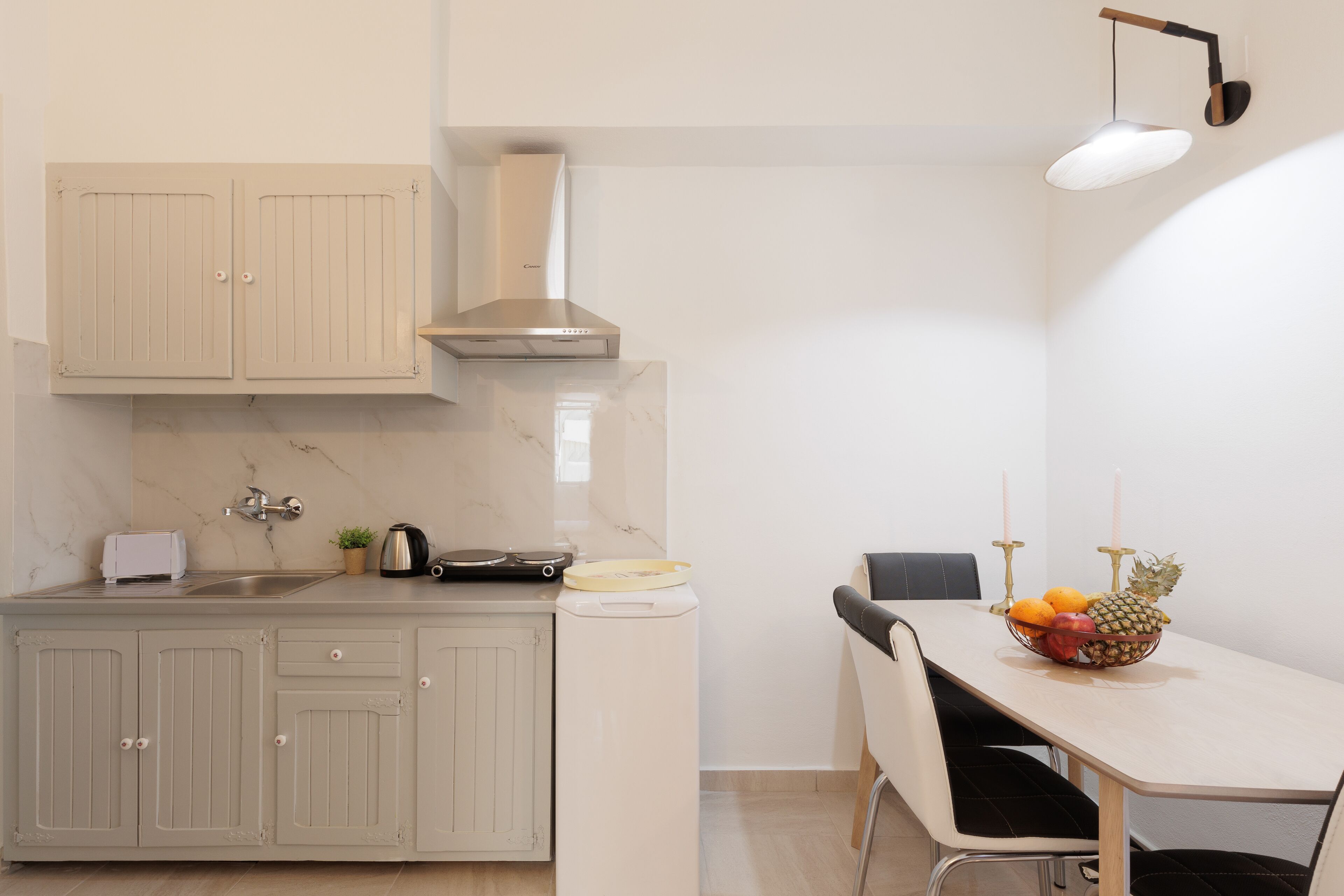 Cocina compacta con lavamanos, estufa y armarios. Hay una mesa de comedor con sillas y un frutero.
