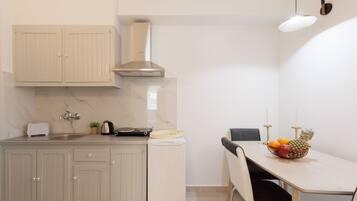 Cocina compacta con lavamanos, estufa y armarios. Hay una mesa de comedor con sillas y un frutero.