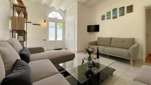 Ein modernes Wohnzimmer mit einem Glastisch, beigen Sofas, einem Flachbildfernseher und einem Bücherregal.