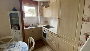 A compact kitchen with wooden cabinets, a sink, a stove, and a dining table with chairs.