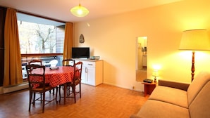 Ein gemütliches Wohnzimmer mit Holzboden, einem Esstisch mit Stühlen, einer Couch, einem Fernseher und einer Lampe.
