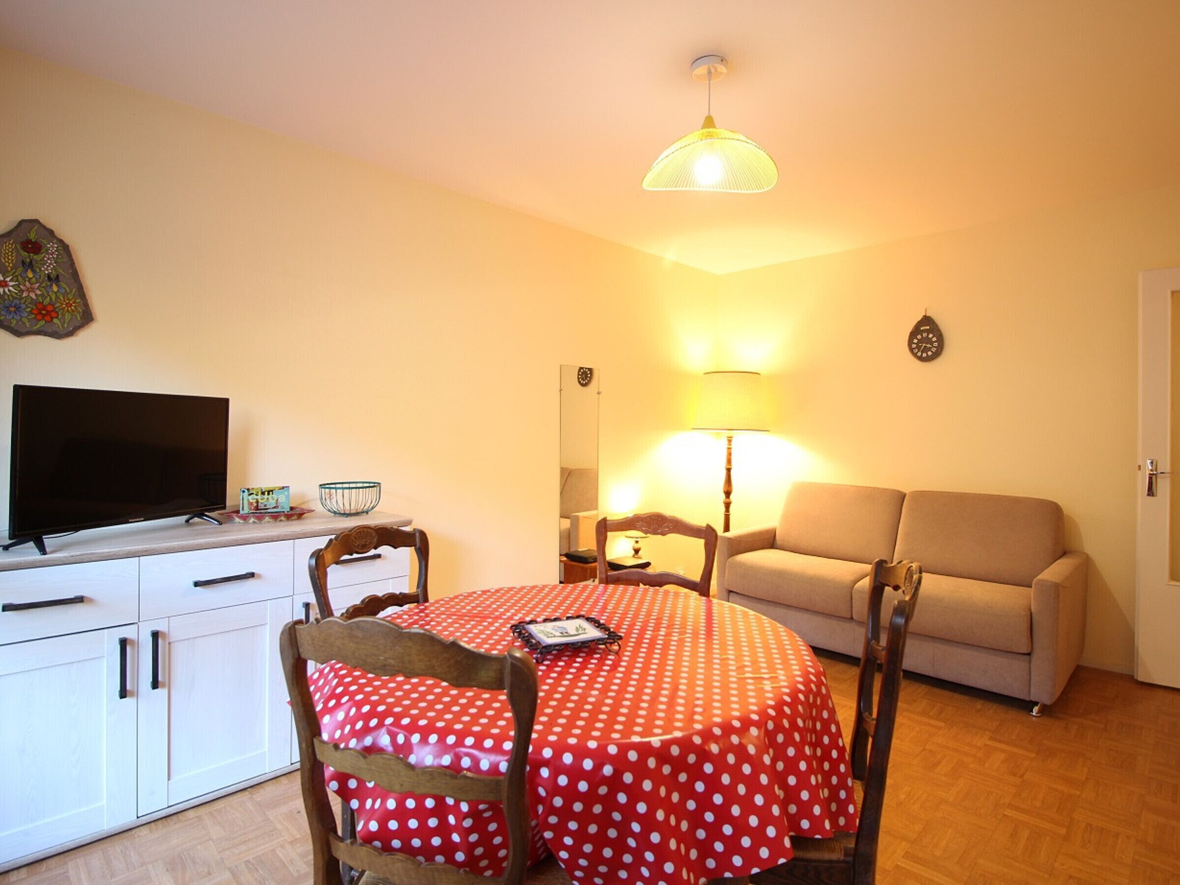 A cozy living room with a television, a dining table with a polka dot tablecloth, a sofa, and a lamp.