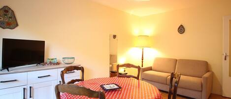 A cozy living room with a television, a dining table with a polka dot tablecloth, a sofa, and a lamp.