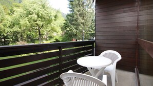 Ein Balkon mit Holzgeländer, zwei weiße Plastikstühle und ein kleiner runder Tisch.