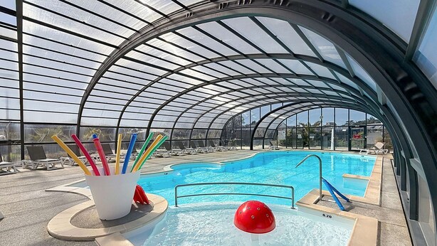 Una piscina con techo de vidrio, sillones de descanso y una fuente de agua roja.
