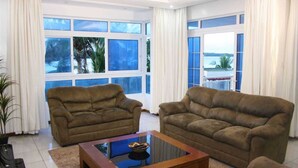 A living room with two brown sofas, a glass coffee table, and large windows with a view of the sea. - Stay.Plus Almasi Beachfront Apartments (Mombasa)