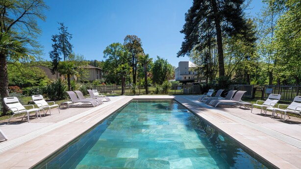 A rectangular swimming pool with clear water, surrounded by lounge chairs and trees.