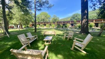 Zona exterior amb gespa, amb bancs de fusta i una taula de picnic, envoltada d'arbres i un edifici al fons.